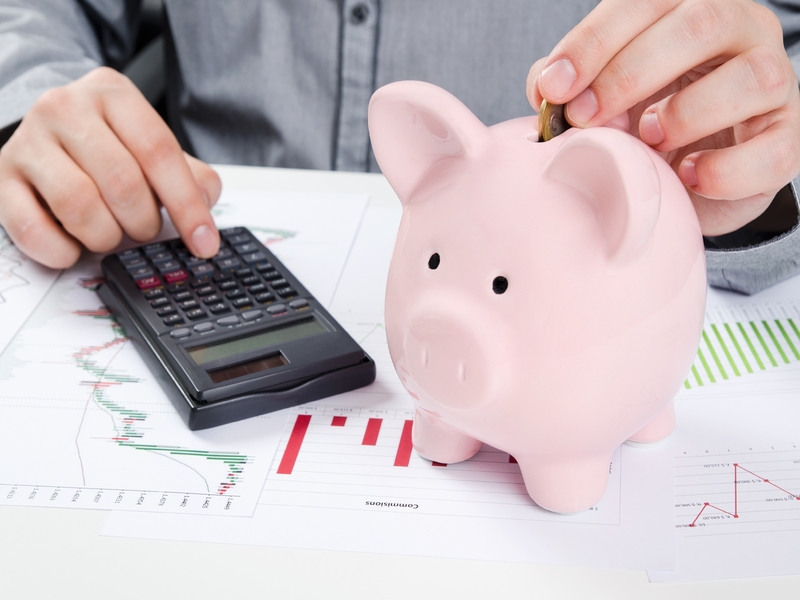 Un homme tapant sur une calculette, une tirelire à côté de lui.