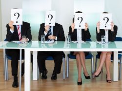 Des hommes et femmes d'affaire assis à une table tenant une feuille avec un point d'interrogation devant le visage.