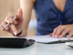 Une femme à une table avec une calculette, calculant les impôts.