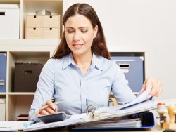 Une femme d'affaire avec un classeur ouvert sur son bureau et une calculette.