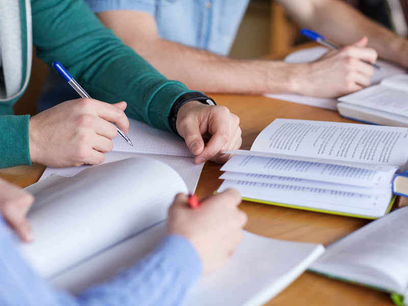 Trois jeunes personnes penchées sur des cahiers sur une table.