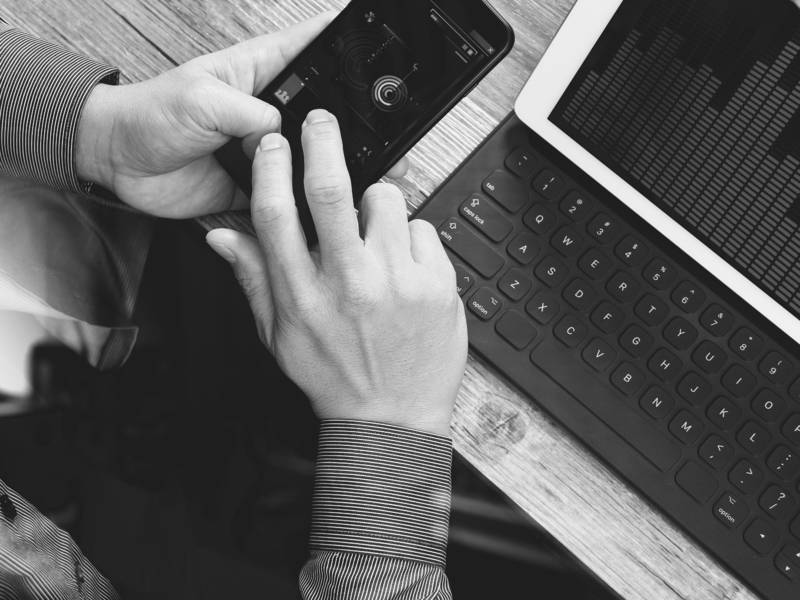 Image en noir et blanc d'une personne assise devant une table qui pianote sur son téléphone.