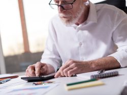 Un homme d'affaire avec une calculette à un bureau sur lequel sont posés des documents.