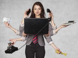 Une femme d'affaires devant un ordinateur. Elle a plusieurs mains, trois d'entre elles tiennent un téléphone, une autre une calculette, une un billet et la dernière une clé à molette.