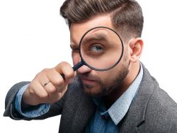 Un homme en costume avec une loupe posé contre l'oeil gauche.