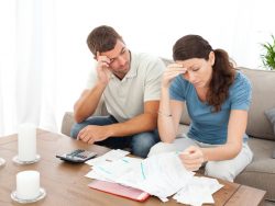 Un couple désespéré devant des feuilles de compte, une calculette est posée sur la petite table devant eux.