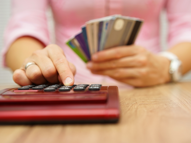 Une femme tenant trois cartes de crédit dans une main et tapant sur une calculette de l'autre.