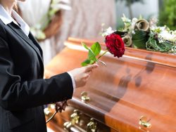 Une femme devant un cercueil avec une rose rouge.