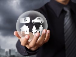 Homme d'affaire tenant une boule où sont représentés les piliers de l'assurance: automobile, immobilier, famille et argent.
