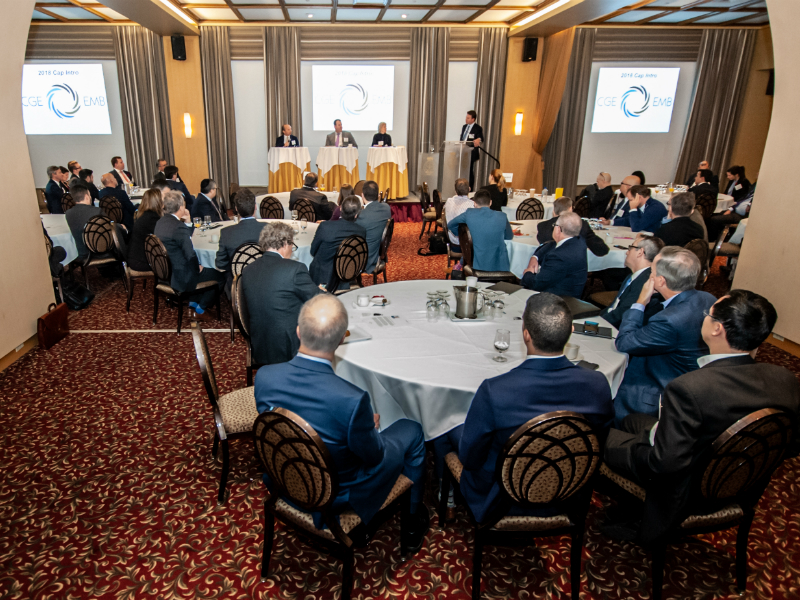 Une association de gestionnaires émergents assis à des tables et regardant vers la scène où se trouvent trois panellistes