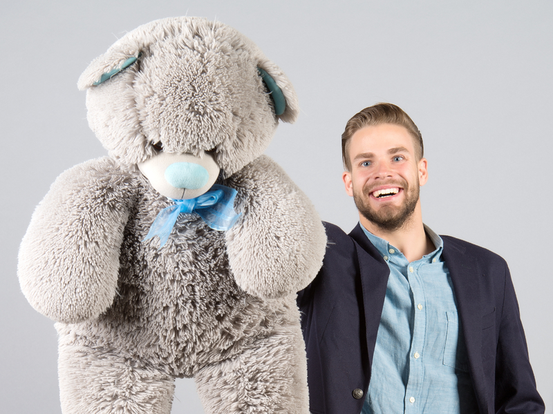 Homme souriant qui tend un gros ours en peluche.