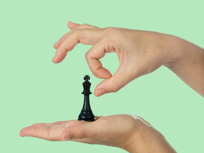 Une personne qui tient le roi d'un jeu d'échec dans une main et s'apprête à lui donner une pichenette de l'autre main.