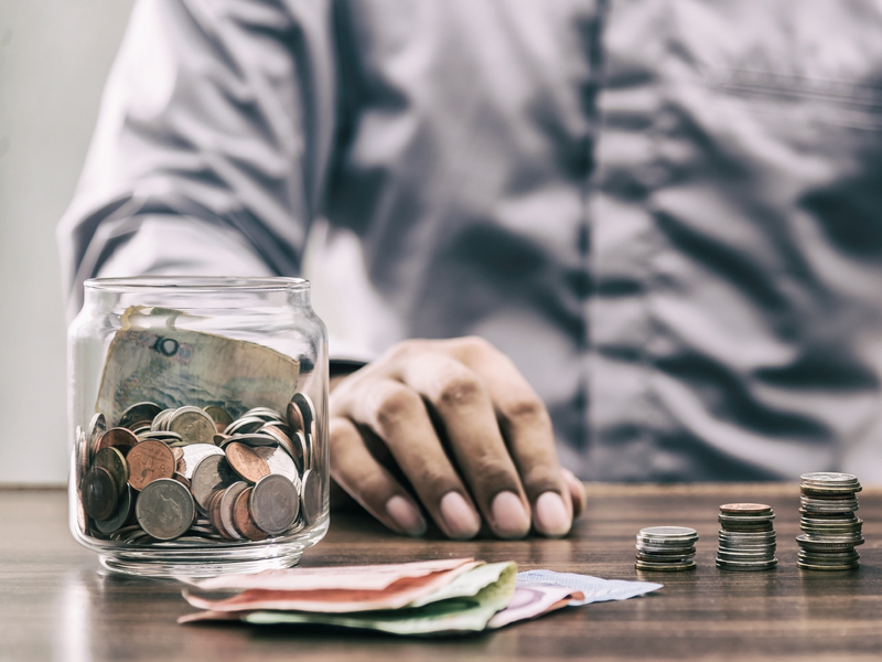 Un homme assis à une table devant un pot plein de monnaie et de la monnaie placée en petits tas devant lui.