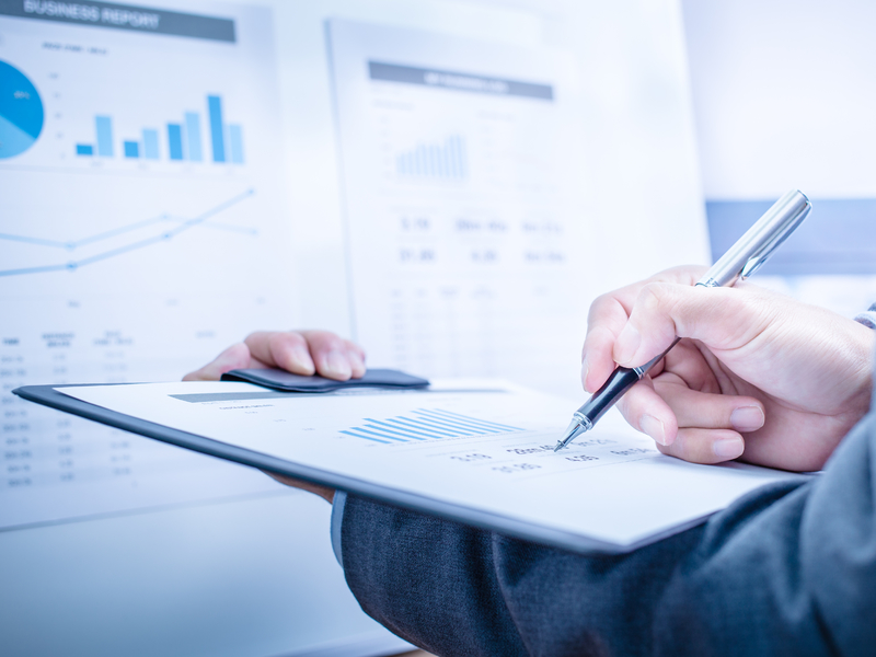 Homme d'affaire tenant une feuille face à un tableau représentant des graphiques financiers.