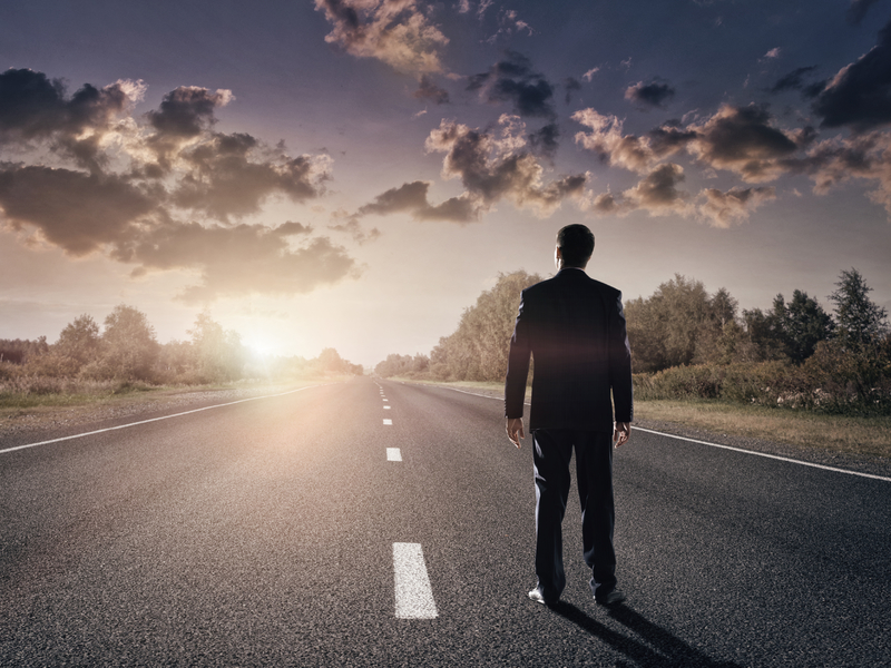 Homme d'affaire sur une route droite face à un soleil levant.