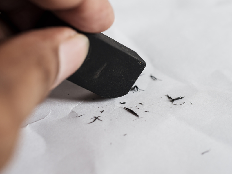 Un homme qui utilise une gomme pour effacer un trait de crayon sur une feuille de papier blanc