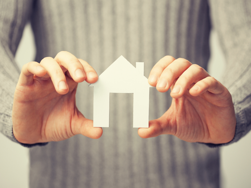 Une femme tenant une maison en papier entre ses mains.