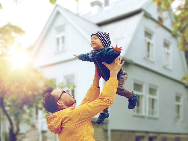 Un père qui tient son enfant à bout de bras devant une maison.