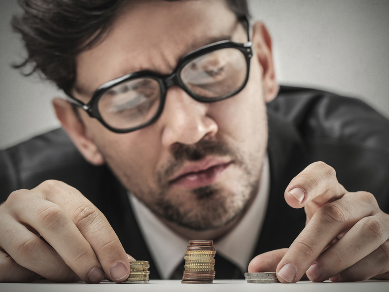 Un homme d'affaire avec des lunettes qui regarde trois petits tas d'argent de taille différente posés sur son bureau, avec circonscription.