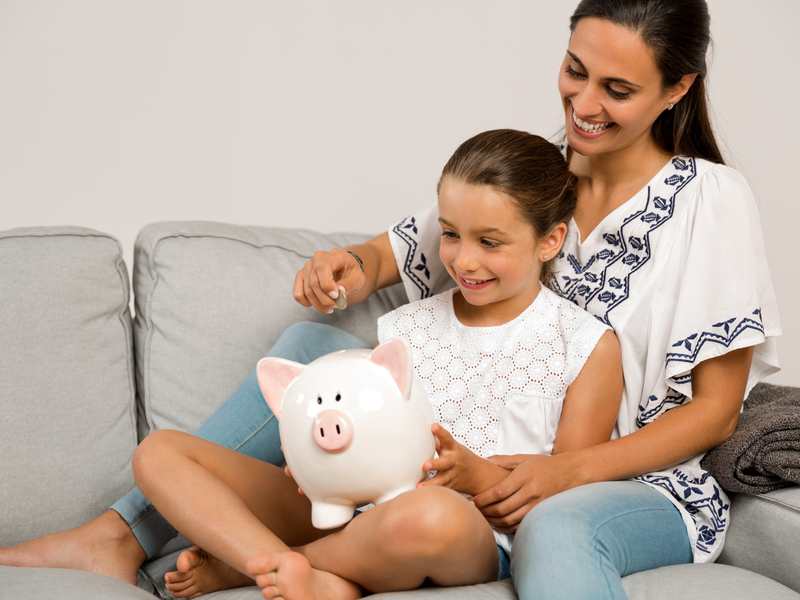 Une femme avec un enfant entre ses jambes assis sur un sofa. Elle met une pièce dans la tirelire sur les genoux de l'enfant.