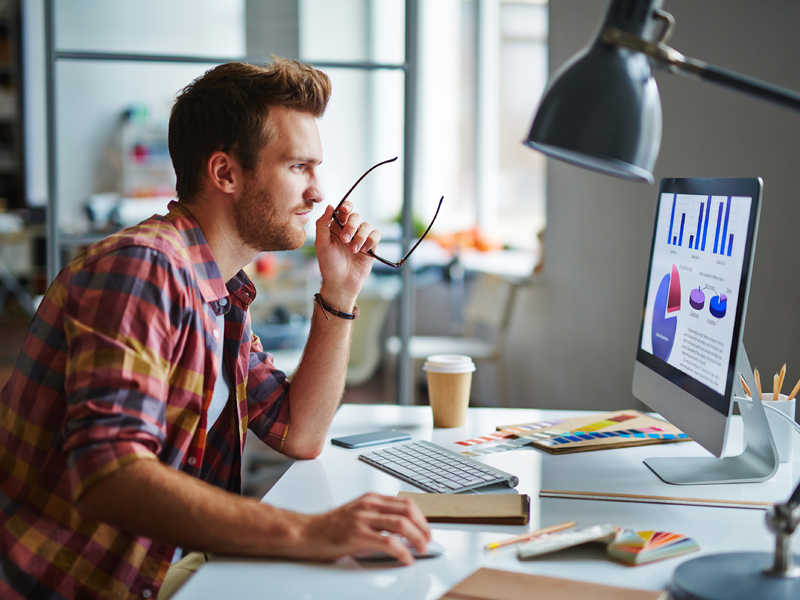 Un homme d'affaire à un bureau, l'air heureux devant un ordinateur lui présentant des graphiques.