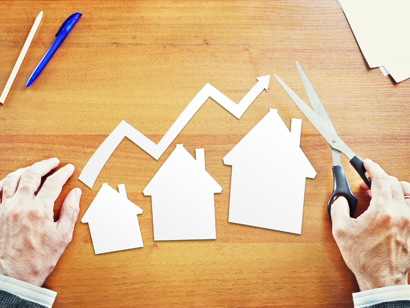 On voit simplement les mains d'un homme d'affaire avec des ciseaux, devant lui trois maisons en papier de plus en plus grandes posées sur une table. Au-dessus, une flèche également en papier montre la croissance.