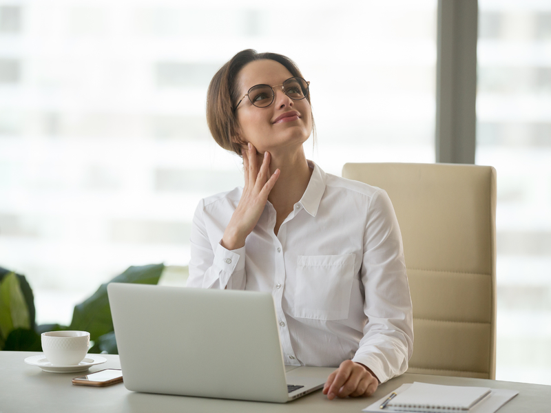 Une femme d'affaires à un bureau. Elle a l'air rêveuse.