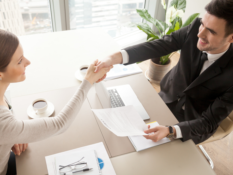 Un homme face à une femme à un bureau dans un contexte de travail. Ils se serrent la main.