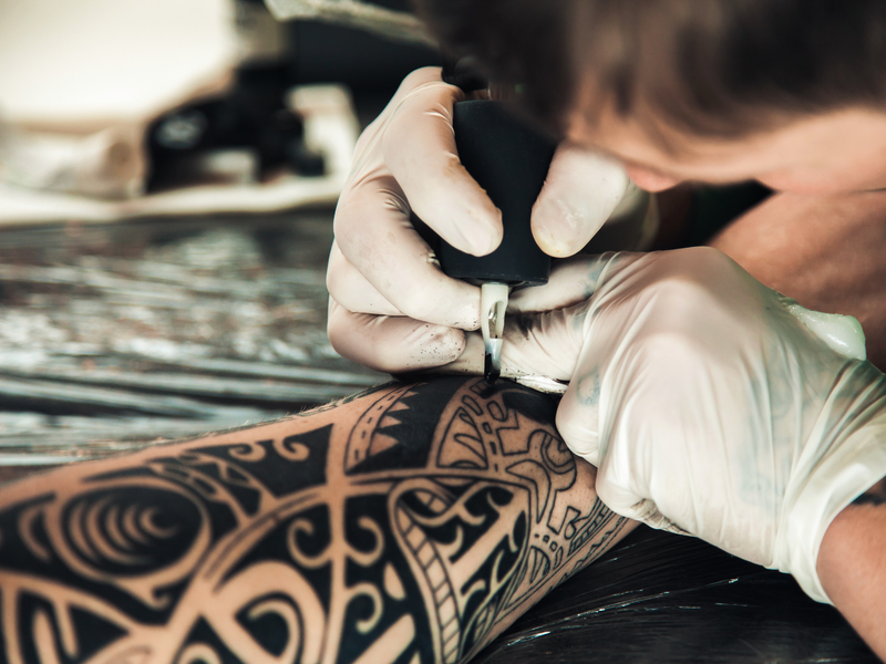 Un tatoueur qui tattoo un bras.