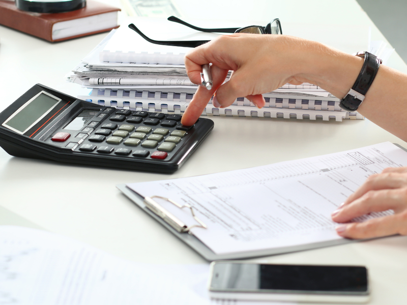 La main d'une femme tapant sur une calculette posée sur une table.