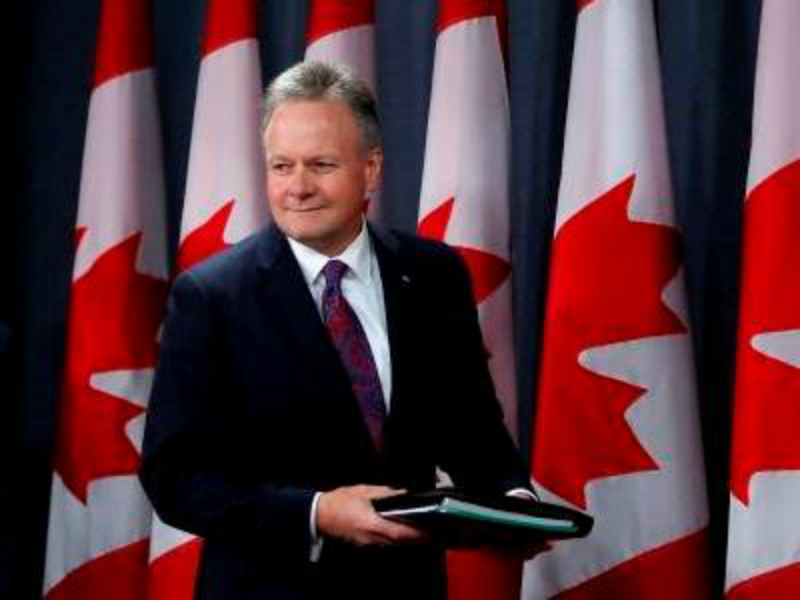 Une photo de Stephen Poloz devant des drapeaux du Canada.