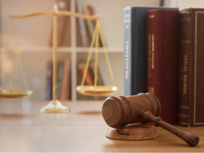 Un marteau judiciaire sur un bureau et une balance de droit avec des livres de droit à côté.