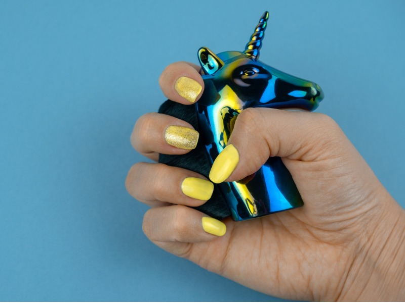 Une femme aux ongles jaunes qui tient une petite tête de licorne en plomb.