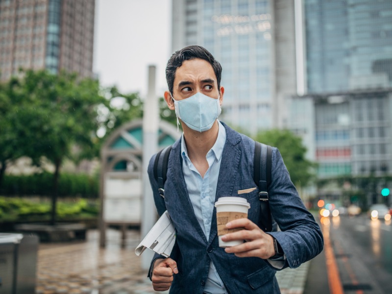 Un homme d'affaires portant un masque. Il a également un café et un journal dans les mains.