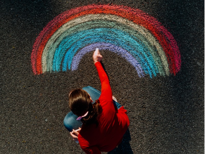 Une femme dessinant un arc-en-ciel sur le sol.