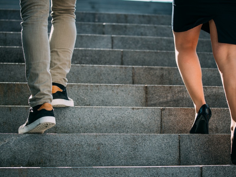 Une femme et un homme grimpant les escaliers. La femme est une marche en dessous de l'homme.