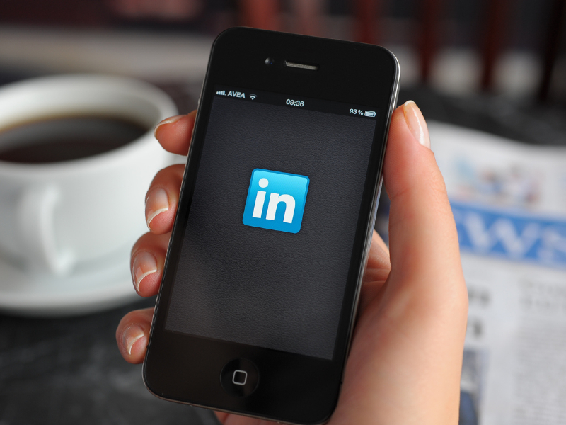 Une personne tenant son téléphone sur lequel on voit le logo de LinkedIn