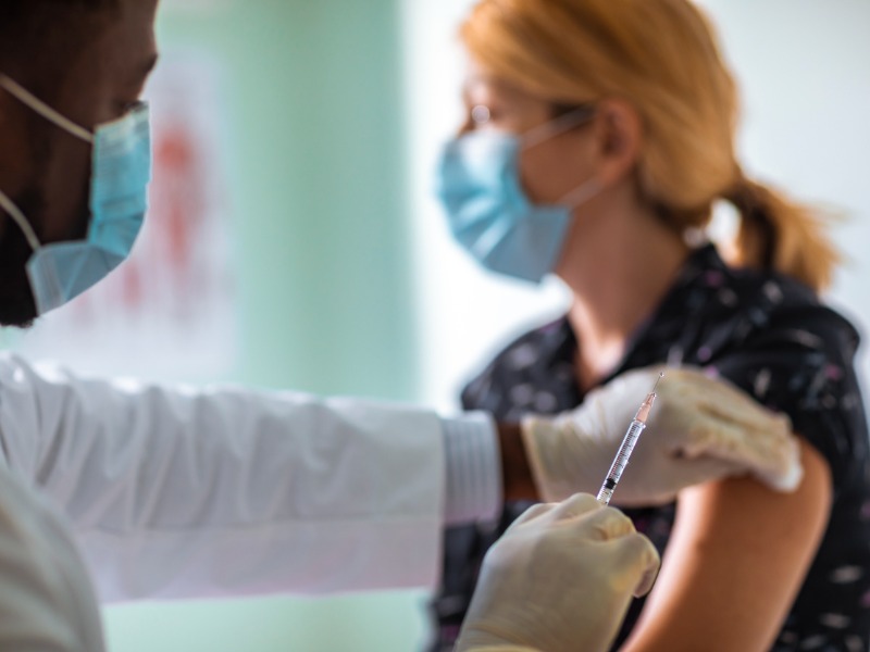 Une femme portant un masque se faisant vacciner par un infirmier portant également un masque.