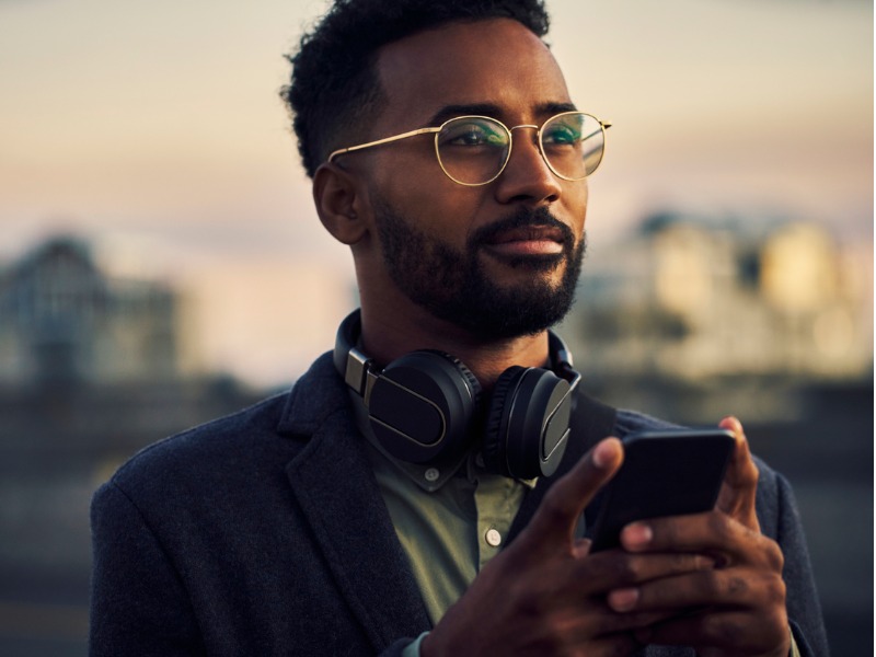 Un homme avec des écouteurs autour du cou qui regarde au loin, son téléphone dans les mains.