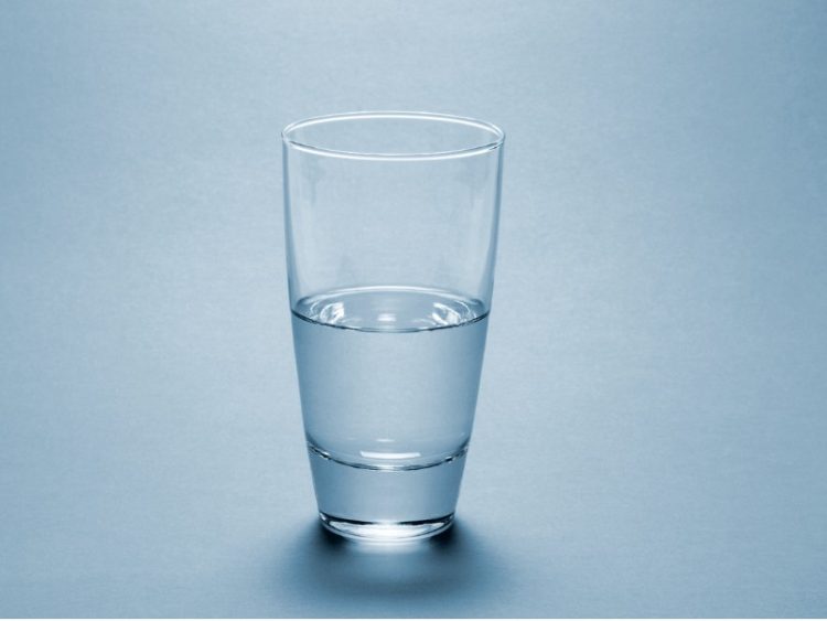 Un verre à moitié rempli d'eau sur un fonds bleu très pâle.