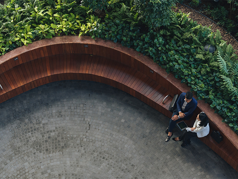 Vue d’en haut d'un homme et d'une femme en tenue d'affaires en conversation réfléchie, assis sur un banc parmi des plantes.