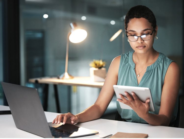 Woman on laptop and tablet around a desk reading finance portfolio.