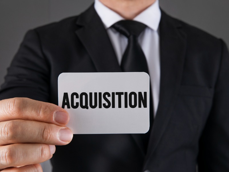 Un homme d'affaire tenant un carton dans les mains. Il y est inscrit acquisition.