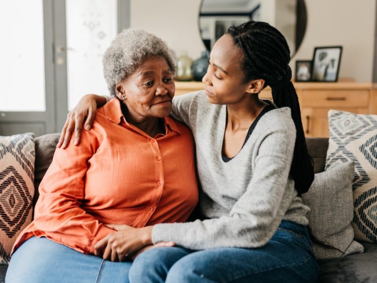Jeune femme étreignant et réconfortant sa mère sur un canapé à la maison.