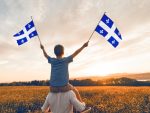 Père et enfant patriotes agitant des drapeaux québécois au coucher du soleil.