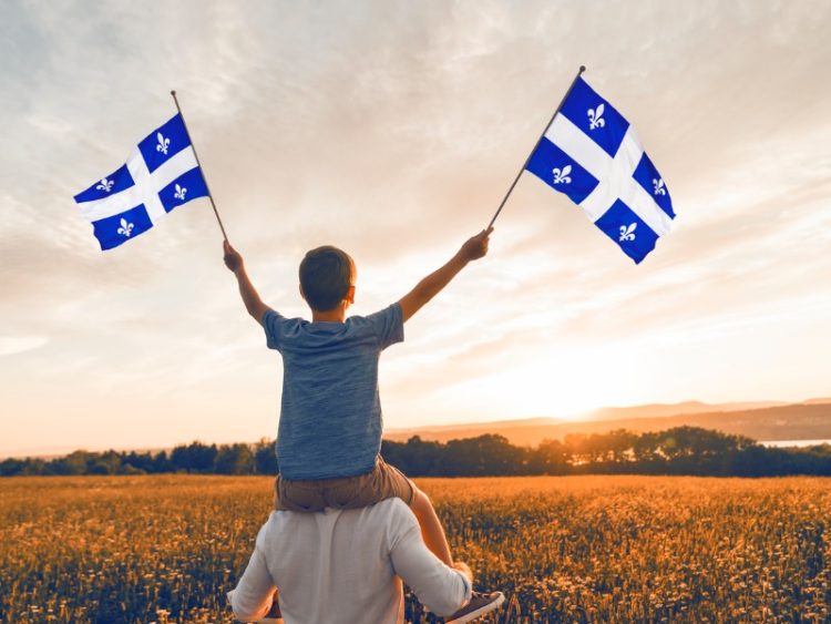Père et enfant patriotes agitant des drapeaux québécois au coucher du soleil.