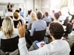 Une salle remplie de personnes prenant des notes en face de quelqu'un qui semble donner une conférence.