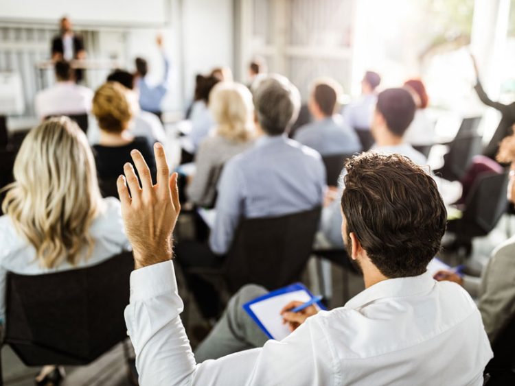 Une salle remplie de personnes prenant des notes en face de quelqu'un qui semble donner une conférence.