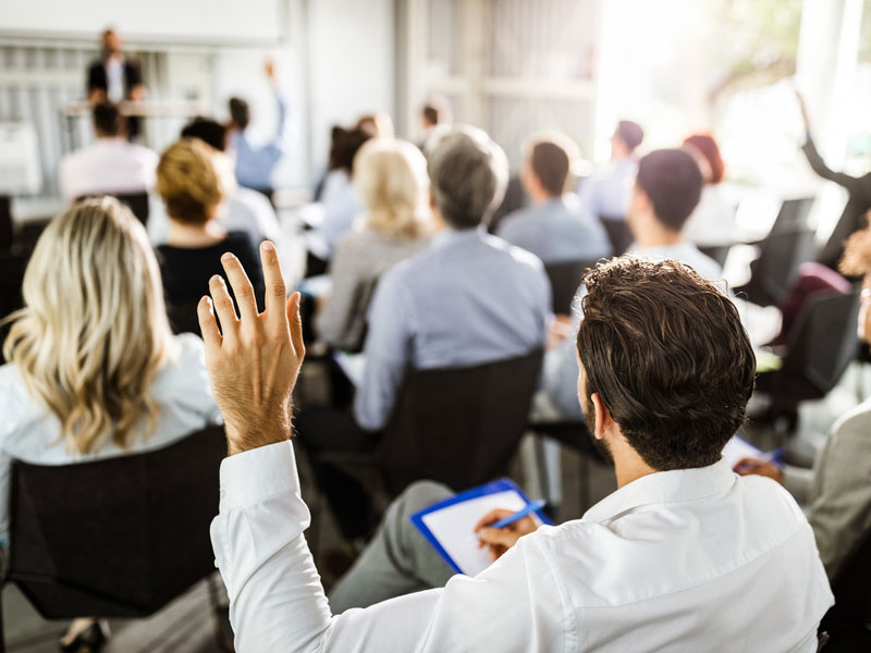 Une salle remplie de personnes prenant des notes en face de quelqu'un qui semble donner une conférence.