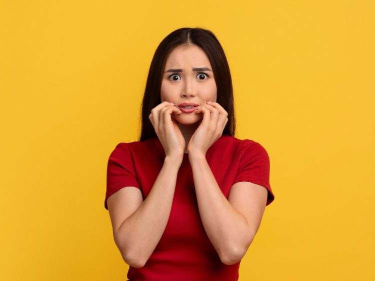 Jeune femme asiatique effrayée touchant son visage, fond de mur jaune.